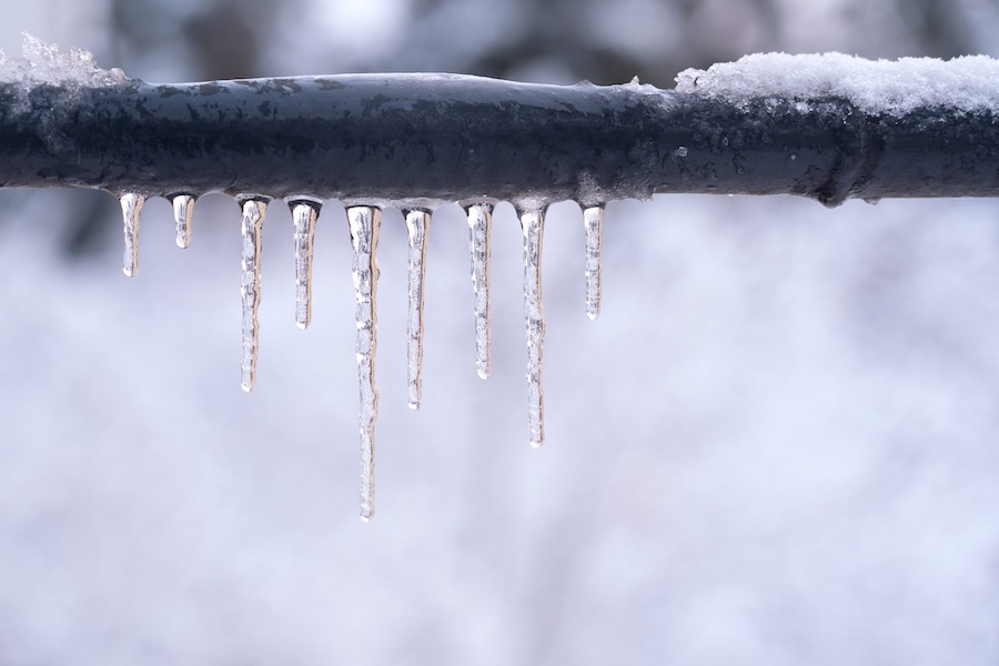 Frozen icicles on a gray pipe after a thaw in winter.